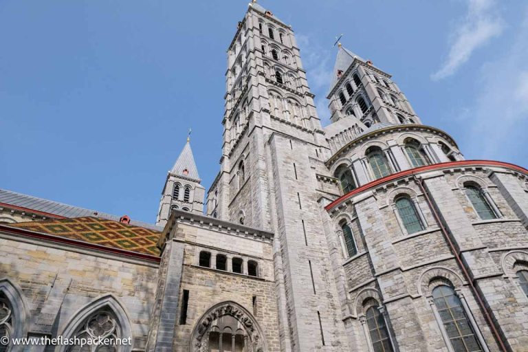 grey stone exterior of tournai cathedral with tiled roof and steeples and bell tower