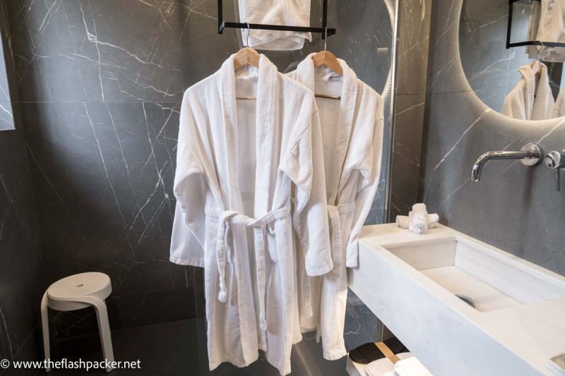 2 bathrobes hanging in a grey marble tiled bathroom