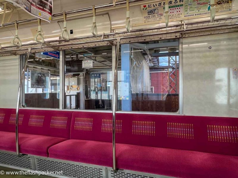 interior of a local japanese train with a long row of seats covered in red frabric