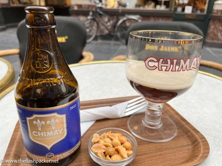 bottle of chimay beer, a glass and bowl of nuts