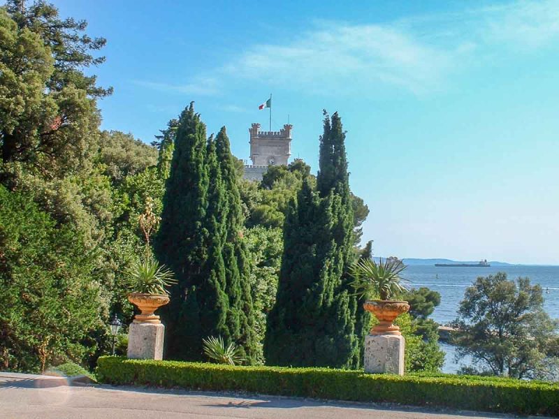 cypress trees and castle tower in front of a blue sea 