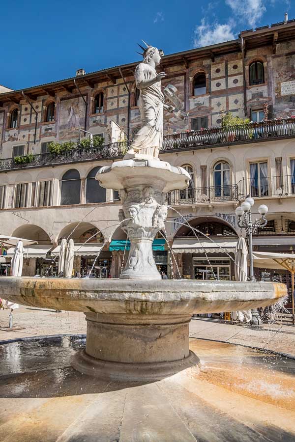 fountain in a piazza del erbe in verona lined with porticoed medieval buildings