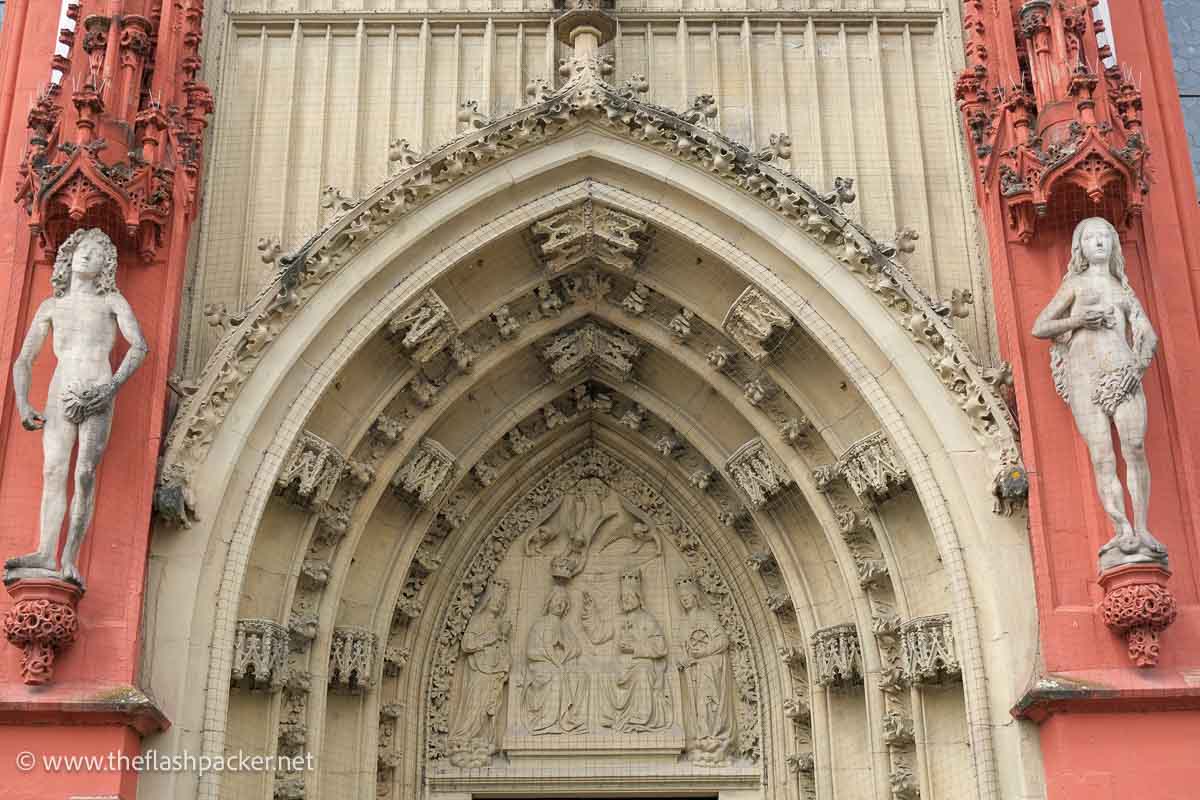 stone carvings over the doorway of the mary church in wurzburg flanked by statues of adam and eve