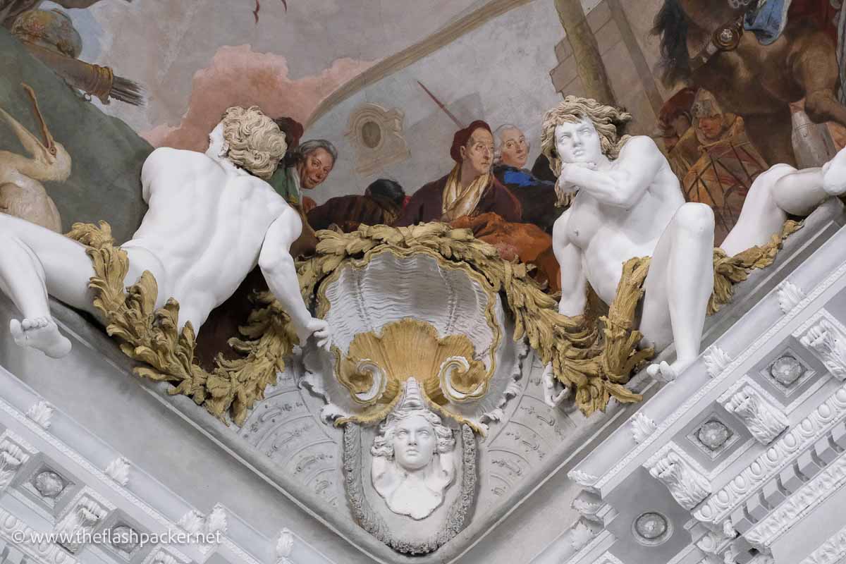 white marble sculptures flanking the corner of a frescoed ceiling